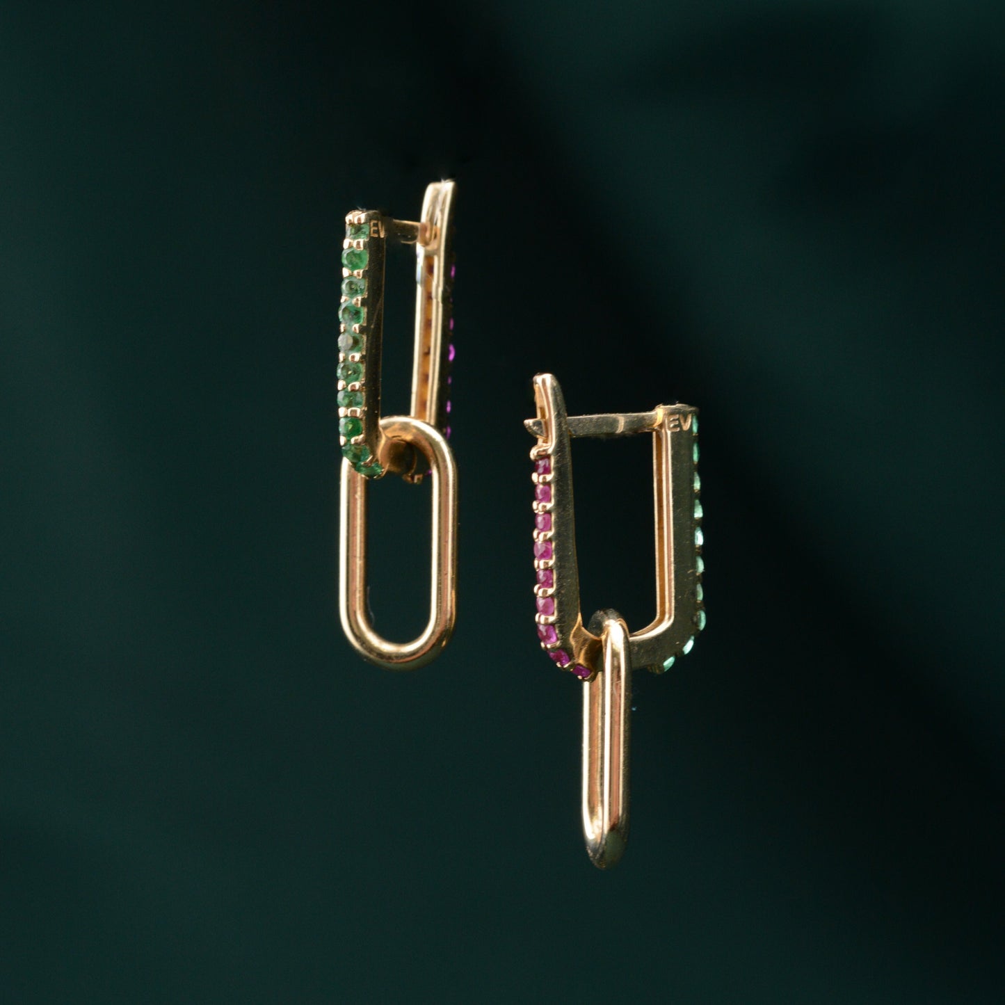A pair of gold earrings featuring emerald and sapphire stones, displayed against a green background.