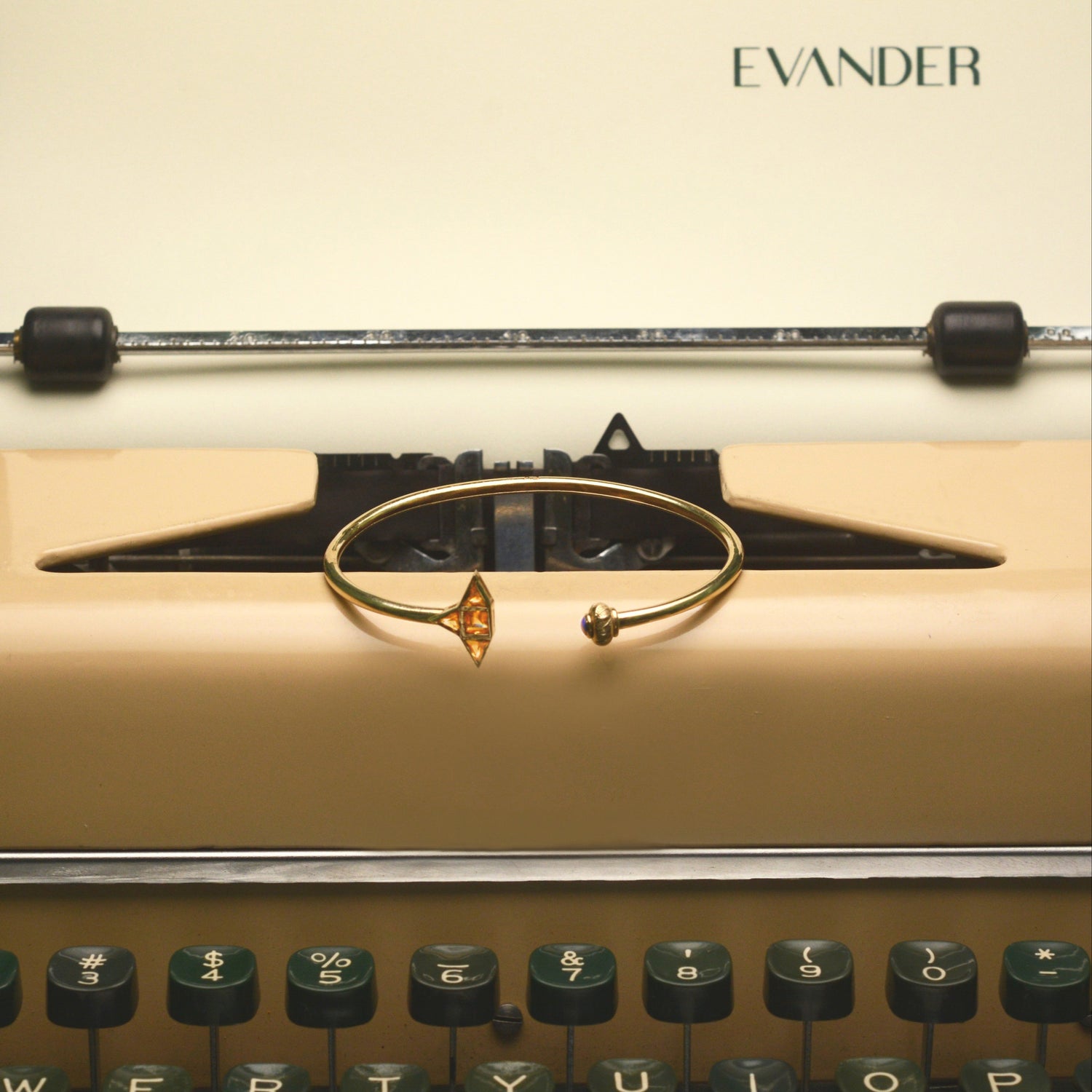 Vintage typewriter with a gold bracelet on top, featuring the brand 'Evander'.