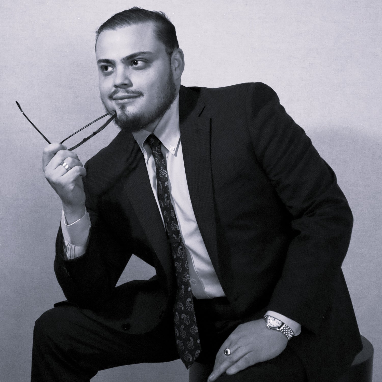 Cesar in a suit holding eyeglasses against a plain background