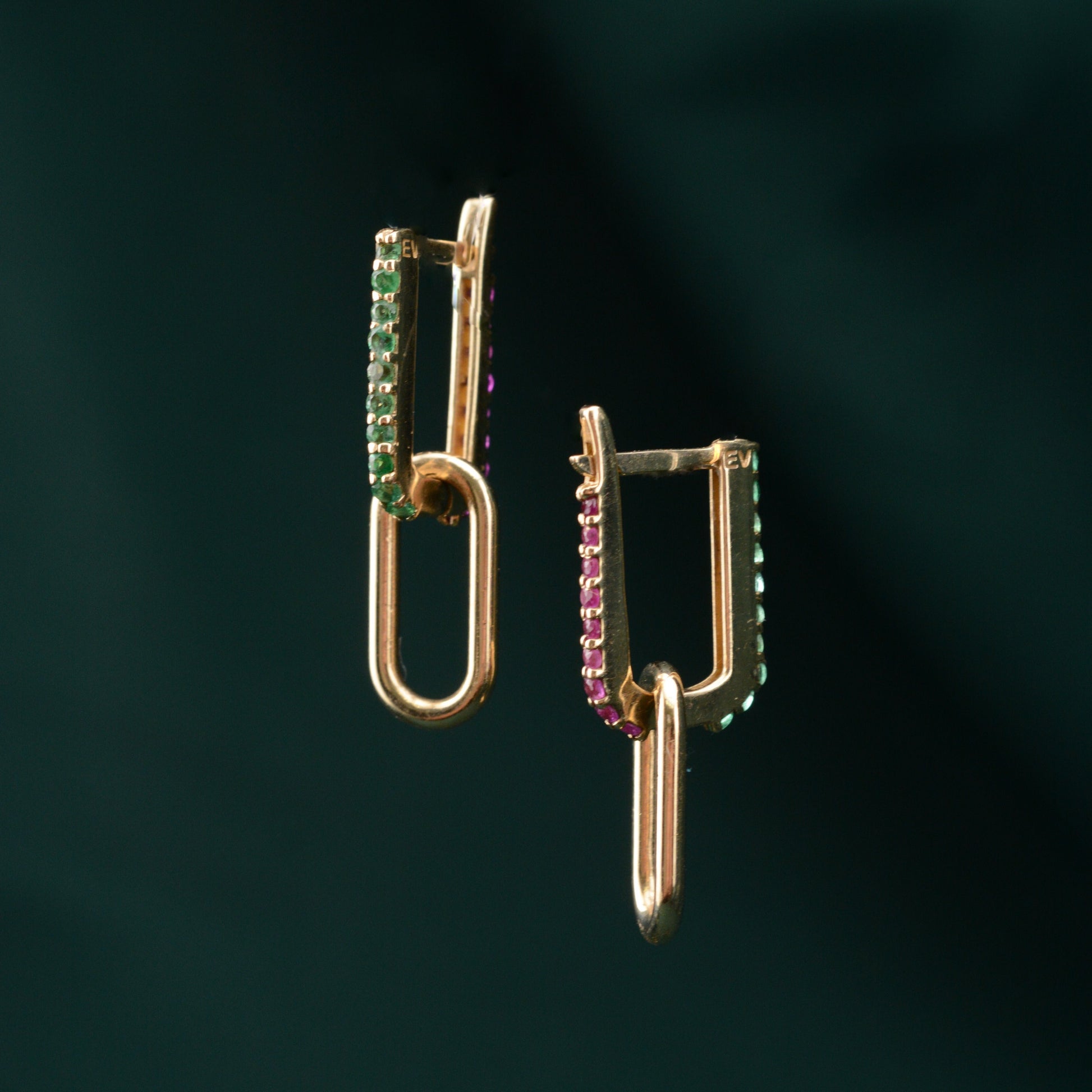 A pair of gold earrings featuring emerald and sapphire stones, displayed against a green background.