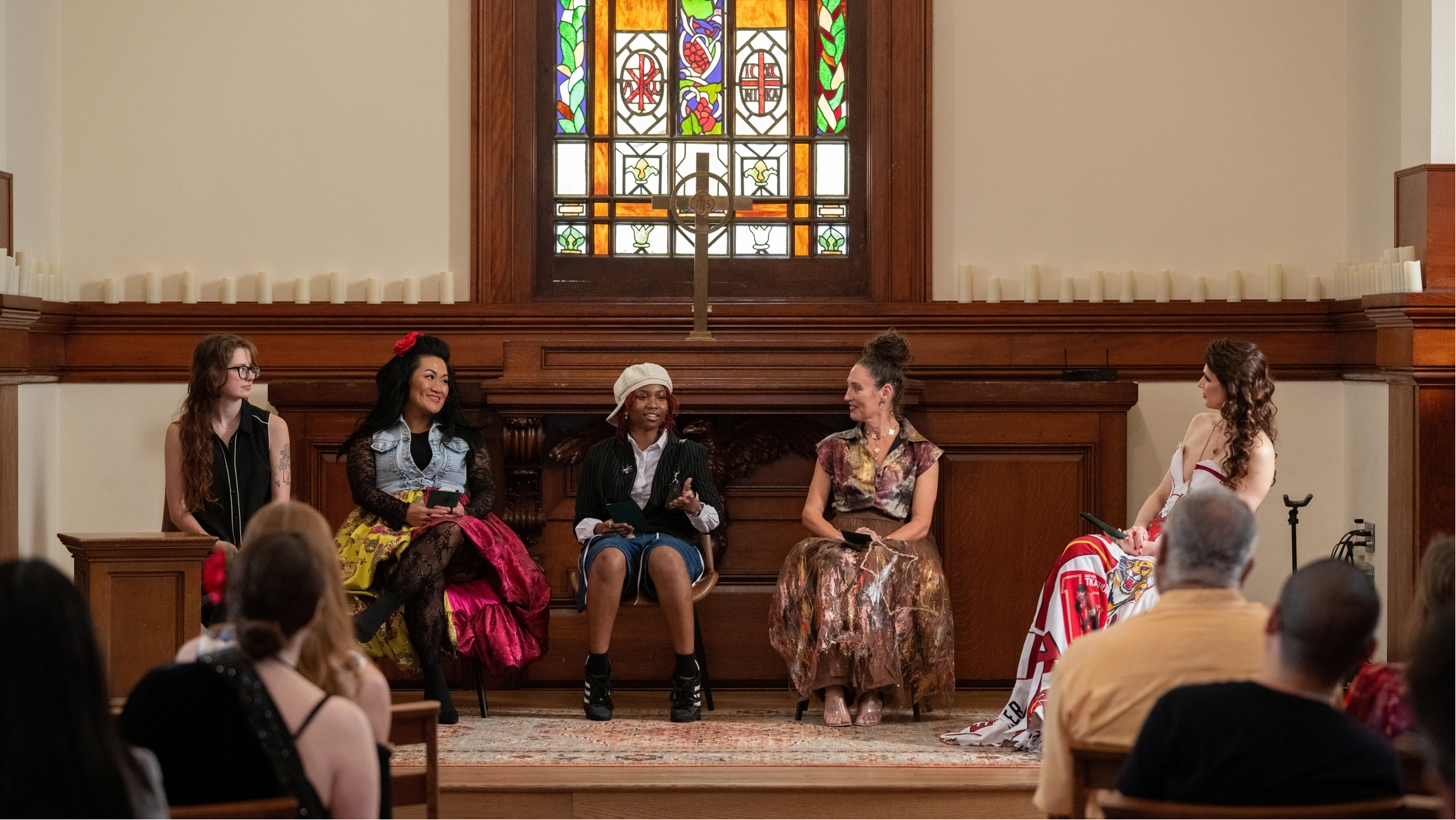 Group of people sitting on a stage with a stained glass window in the background