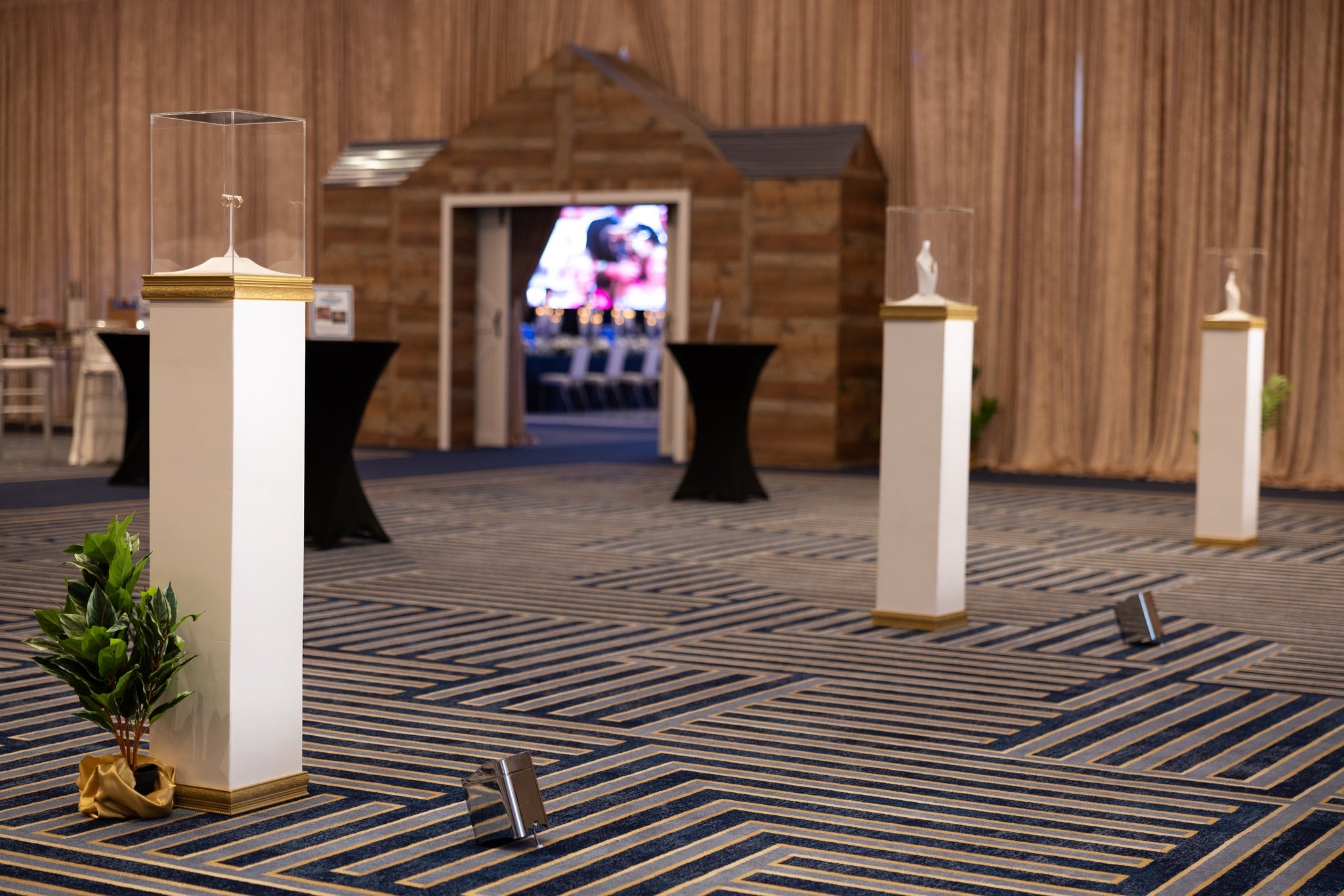 Decorative setup with white columns and gold bases in a room with wooden walls and striped carpet.