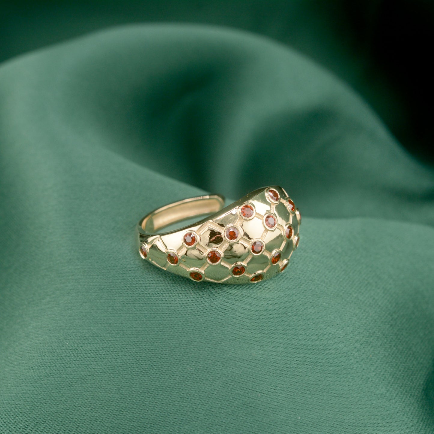 Lattice hoop earrings with red gemstones on a green fabric background