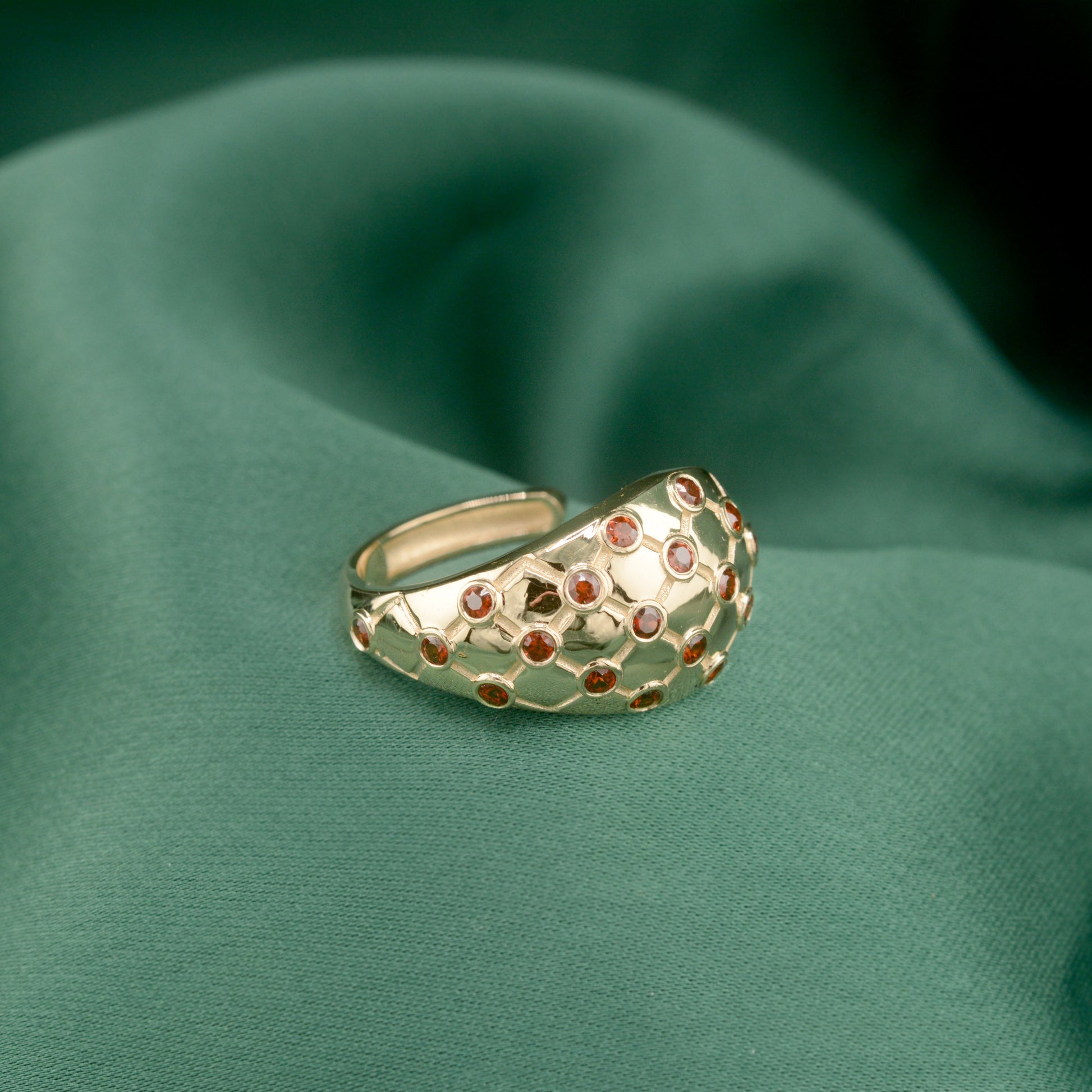 Lattice hoop earrings with red gemstones on a green fabric background