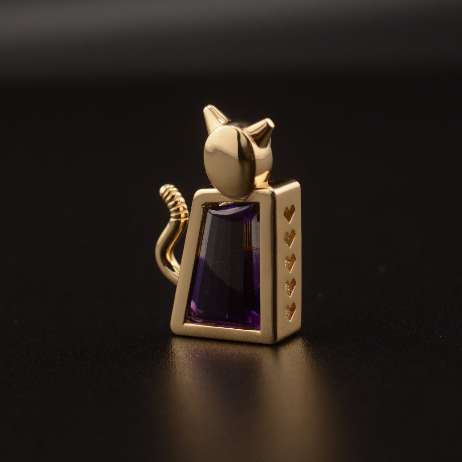 Gold cat-shaped pendant with an amethyst gemstone on a black background