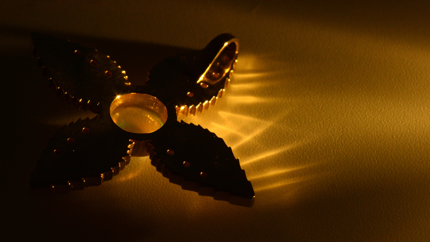 Dark metallic object with a central circular component on a gold background